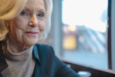 Lächelnde ältere Frau sitzt am Fenster eines Cafés - AMWF00173