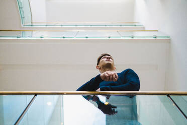 Young man leaning on railing at corridor - AMWF00180