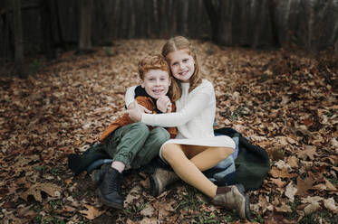 Mädchen umarmt Bruder auf Herbstblättern sitzend - ELEF00041
