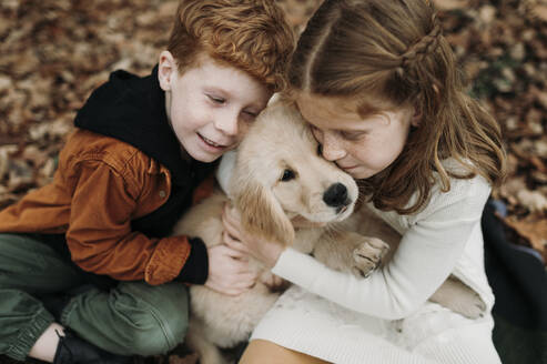 Siblings embracing golden retriever puppy in forest - ELEF00044