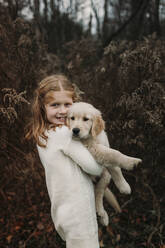 Lächelndes Mädchen mit Golden Retriever Welpe vor einem Baum stehend - ELEF00049