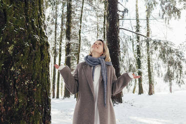 Frau mit Schal steht an einem Baum im verschneiten Wald - OMIF00636