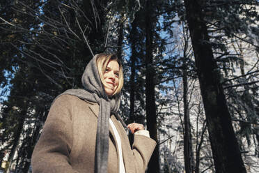 Smiling woman wearing scarf in front of trees at forest - OMIF00642