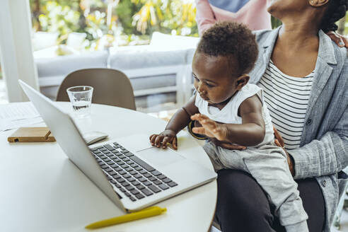 Mutter mit kleinem Jungen auf dem Schoß am Laptop im Esszimmer - MFF08420