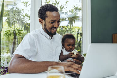 Lächelnder Vater mit Sohn, der einen Laptop im Esszimmer benutzt - MFF08422