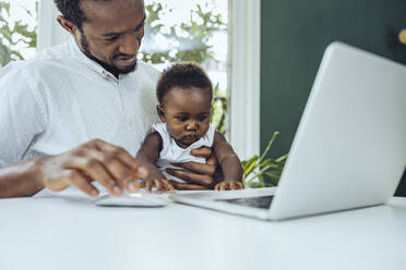 Freelancer with son working on laptop in dining room - MFF08424