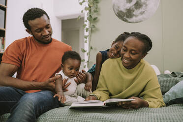 Lächelnde Mutter, die mit ihrer Familie im Schlafzimmer ein Buch liest - MFF08438