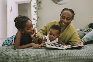 Mutter mit Kindern, die zu Hause auf dem Bett liegen und ein Buch lesen - MFF08439