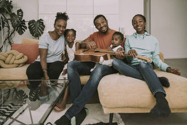 Lächelnde Familie mit Gitarre auf der Couch sitzend - MFF08446