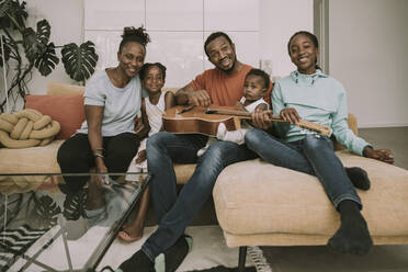 Smiling family with guitar sitting on couch - MFF08446