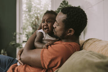 Father calming down baby boy crying in living room - MFF08461