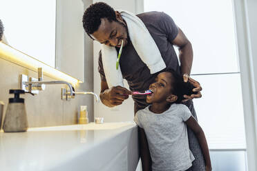 Father brushing teeth of daughter in bathroom at home - MFF08465