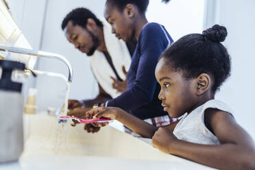 Girl washing toothbrush below running water in bathroom - MFF08468