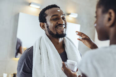 Girl applying face cream to father in bathroom - MFF08477