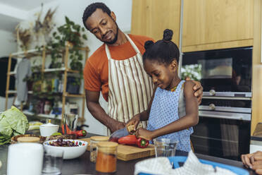 Girl cutting pointed pepper by father in kitchen at home - MFF08489