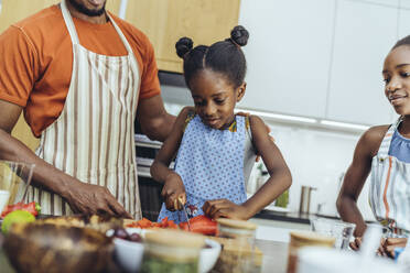 Mädchen schneidet Cayennepfeffer mit Vater und Schwester in der Küche - MFF08490