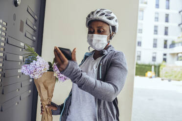 Auslieferungsfrau mit Gesichtsschutzmaske hält Blumenstrauß an der Eingangstür - MFF08505