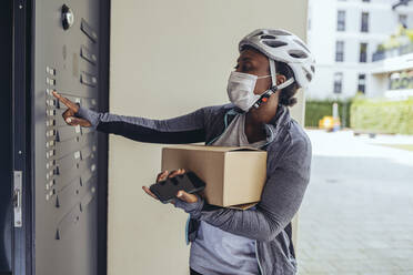 Delivery woman with protective face mask holding package box at entrance door - MFF08507