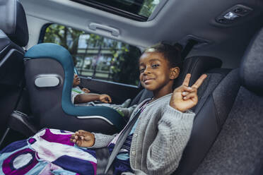 Lächelndes Mädchen mit Friedenszeichen im Auto sitzend - MFF08516