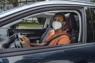 Man in protective face mask driving car in COVID-19 outbreak - MFF08550