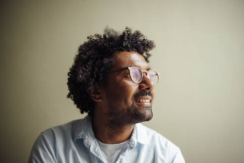 Smiling man with curly hair wearing eyeglasses at wall - GUSF07085