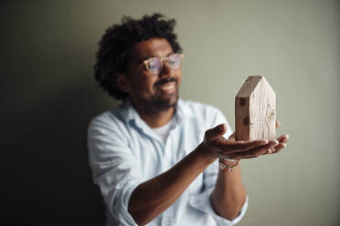 Glücklicher Mann mit Brille betrachtet ein Modellhaus zu Hause - GUSF07093
