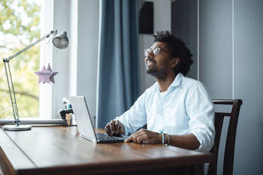 Happy man with laptop sitting at table - GUSF07126