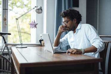 Mann mit Brille sitzt mit Laptop am Tisch - GUSF07127