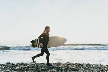 Mann mit Surfbrett läuft am Strand - OMIF00664