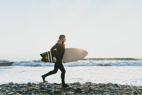 Man with surfboard running on beach - OMIF00664