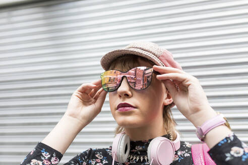 Junge Frau mit Sonnenbrille vor einem geschlossenen Fensterladen - WPEF05812
