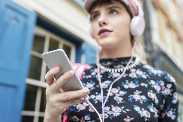 Junge Frau mit Smartphone hört Musik über Kopfhörer - WPEF05815