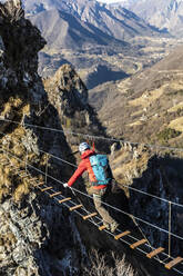 Entschlossener Mann, der auf einer tibetischen Brücke geht, Orobie Alpen, Bergamo, Italien - MCVF00956