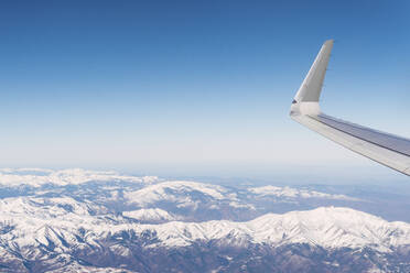 Flugzeug fliegt über schneebedeckte weiße Berge an einem sonnigen Tag - PNAF03257