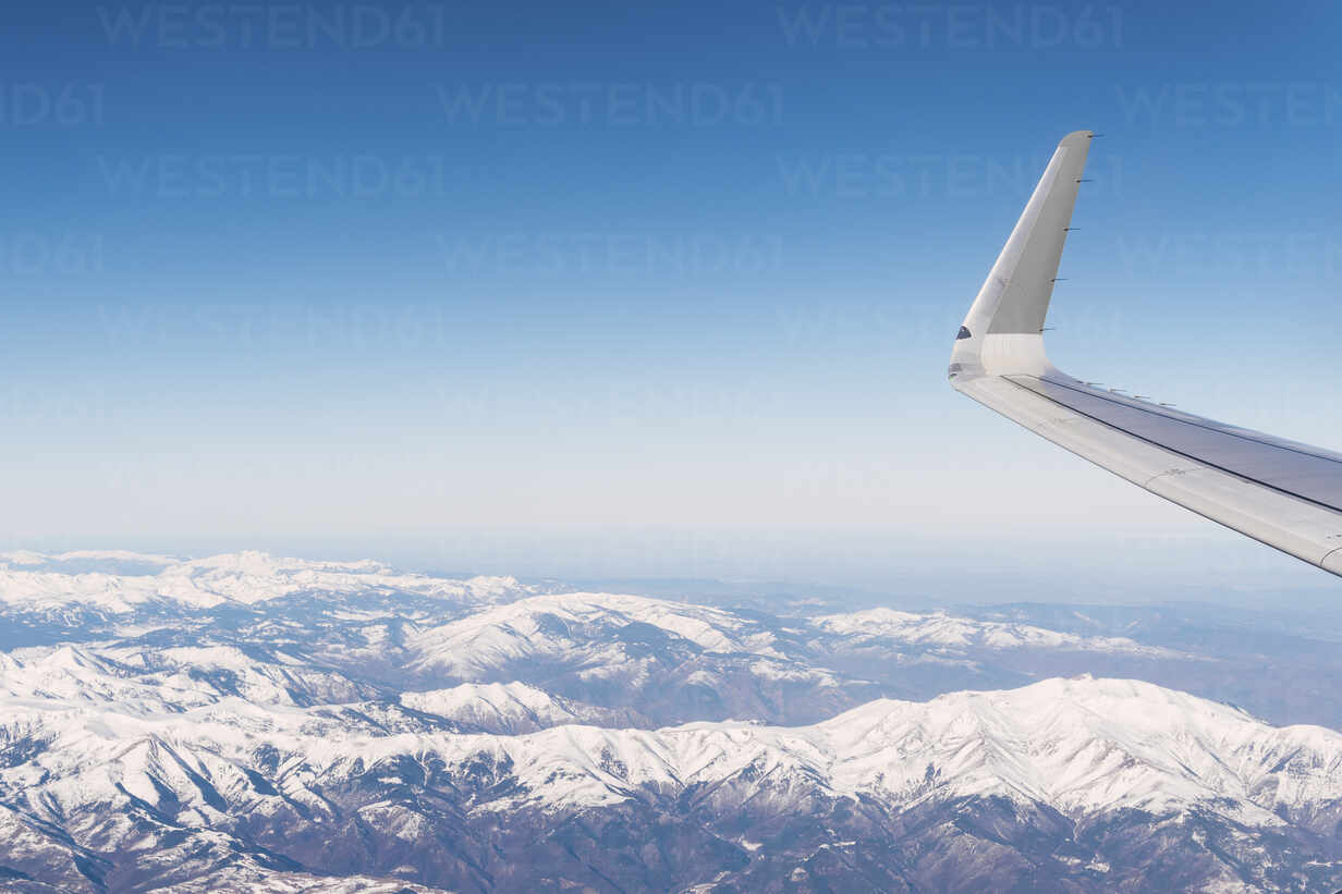 Airplane flying over snow covered white mountains on sunny day stock photo