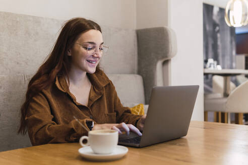 Lächelnde Geschäftsfrau, die in einem Café an einem Laptop arbeitet - PNAF03266
