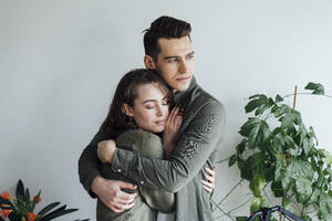 Junger Mann umarmt Freundin mit geschlossenen Augen zu Hause - VPIF05355