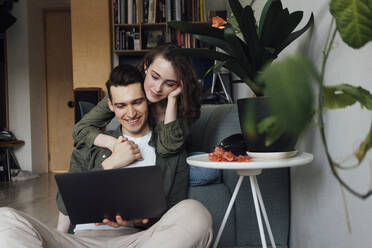 Glückliches Paar hält sich an den Händen und teilt sich einen Laptop im heimischen Wohnzimmer - VPIF05359