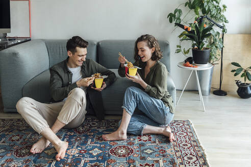 Glückliches junges Paar mit Essen zum Mitnehmen sitzt auf dem Sofa im Wohnzimmer zu Hause - VPIF05378