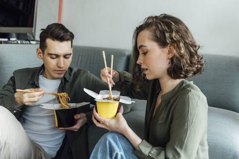 Young couple with chopsticks eating noodles at home - VPIF05381