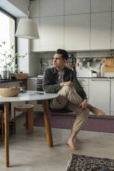 Nachdenklicher junger Mann sitzt am Tisch in der Küche - VPIF05392