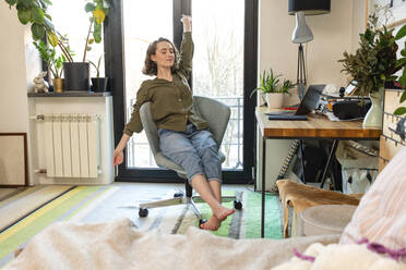 Tired young woman with hand raised sitting on chair at home - VPIF05398