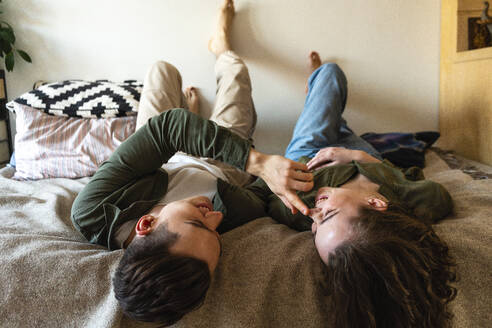 Glücklicher Mann berührt die Nase seiner Freundin auf dem Bett liegend zu Hause - VPIF05406