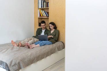 Junges Paar, das sich einen Laptop teilt und zu Hause auf dem Bett sitzt - VPIF05408