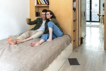 Glücklicher junger Mann nimmt Selfie mit Freundin durch Smartphone im Schlafzimmer zu Hause - VPIF05409