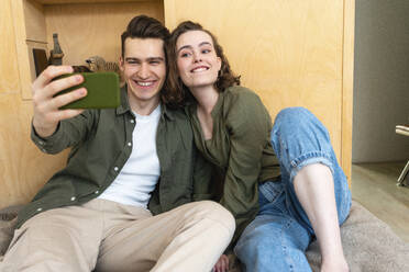 Happy young couple taking selfie through mobile phone at home - VPIF05410