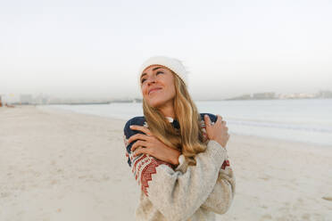 Lächelnde Frau in warmer Kleidung, die sich am Strand umarmt - TYF00078