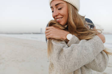 Glückliche Frau mit geschlossenen Augen umarmt sich selbst am Strand - TYF00079