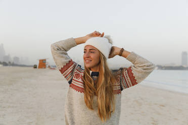 Happy blond woman wearing knit hat at beach - TYF00080