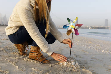 Frau, die ein mehrfarbiges Windrad-Spielzeug in den Sand am Strand legt - TYF00088